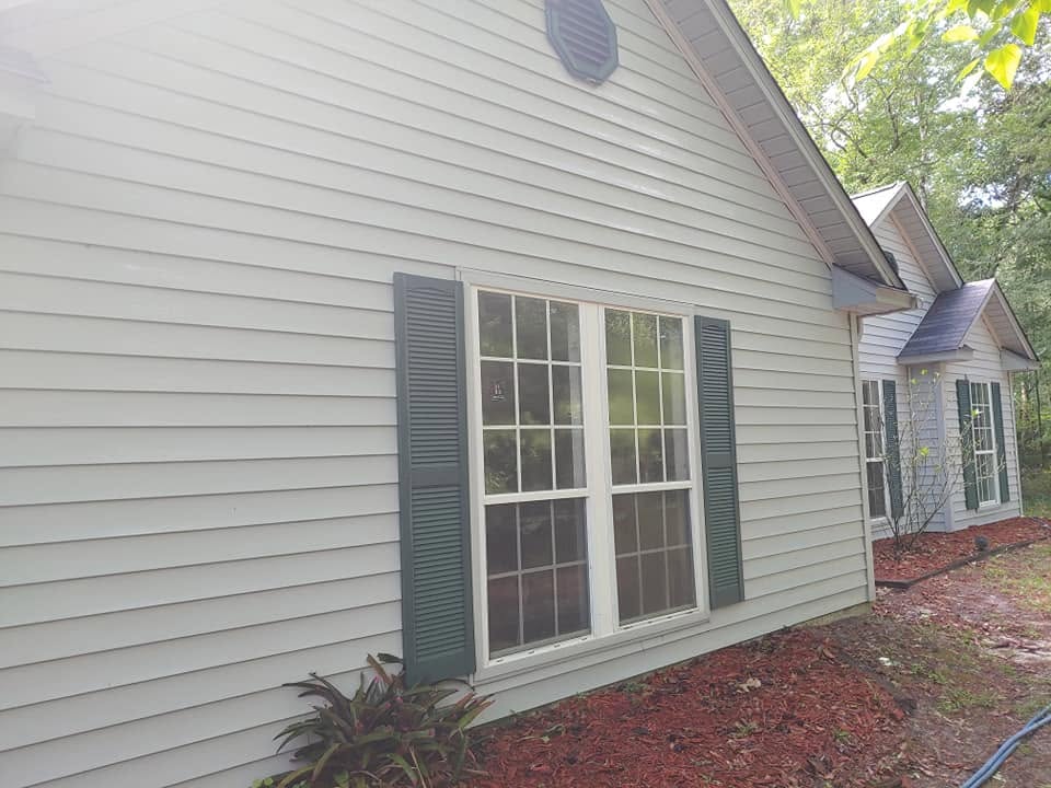 After: the same siding and shuttered window washed back to clean cream, with the staining gone.